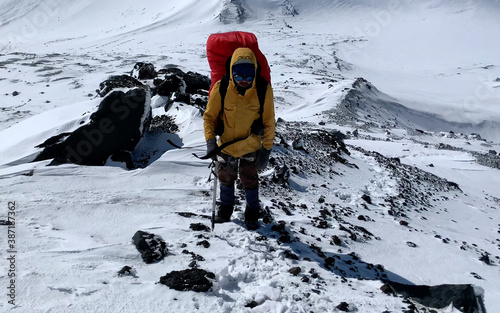 Fotografía Climber in a yellow jacket with an ice ax goes to the top of the volcano along a snow-covered trail