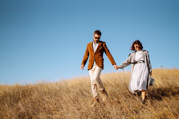 Stylish  young couple enjoying autumn weather in autumn field. Lovely couple walking and hugging in the field together. The concept of youth, love and lifestyle.