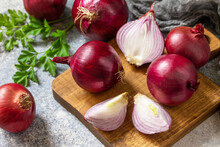 Purple Onions. Fresh Whole Purple Onions And One Sliced Onion On A Stone Countertop.