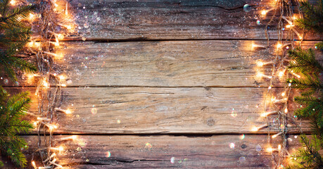 Wall Mural - rustic christmas border - fir branches and string light on old wooden plank with defocused abstract 