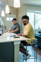 Wall Mural - gay couple working from home on laptop computers sitting at kitchen counter