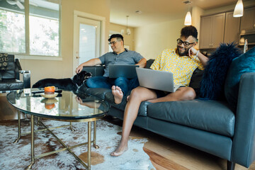 Wall Mural - happy gay couple working from home with laptops on couch with their australian shepherd