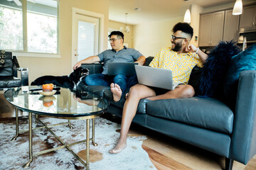 Happy gay couple working from home with laptops on couch with their Australian Shepherd 