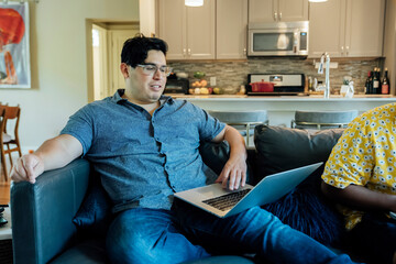 Wall Mural - happy gay couple working from home with laptop computers, sitting on couch