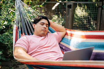 Wall Mural - man relaxing in hammock working on laptop computer