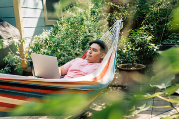 Wall Mural - man relaxing in hammock working on laptop computer