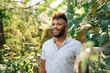 Wall Mural - Portrait of smiling, happy confident black man with mohawk standing outdoors in garden