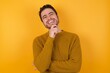 © Roquillo - Young man wearing casual sweater and over isolated yellow background laughs happily keeps hand on chin expresses positive emotions smiles broadly has carefree expression
