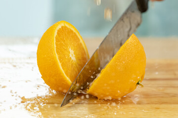 Wall Mural - hands cutting orange with splash of orange juice on wooden cutting board