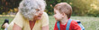 © anoushkatoronto - Grandmother lying on grass with grandson boy at home backyard. Bonding of relatives and generation communication. Old woman with baby together outdoors. Web banner header.
