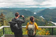 Hikers Couple Camping Walking With Backpacks In Quebec National Park Taking Picture Of View With Phone In Autumn, Canada Forest Travel Lifestyle. Tourists Looking At Jacques Cartier National Park.
