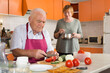 © JackF - Elderly man cooking with his wife at home, cutting fresh vegetables for family dinner
