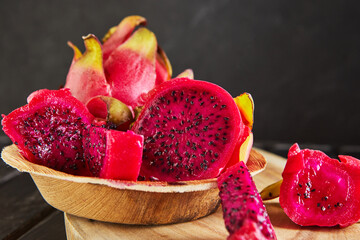 Poster - Dragon Fruit - Pitahaya Cut and one whole on a wooden stand against a black wooden background