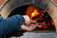 Man Puts Pizza In A Professional Brick Oven With Red Light Due To The Fire Inside The Oven, Soft Focus