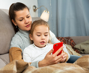 Mom and small daughter using smartphone in home interior