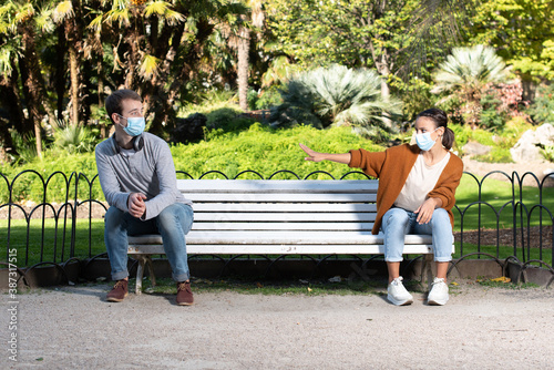 Social distancing during Coronavirus pandemic concept. A young man and woman sitting on a bench of a park and keeping distance to avoid the contagion.