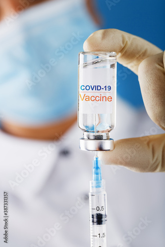 Syringe and ampoule with the inscription COVID-19 vaccine in the hands of a doctor-researcher in rubber gloves with a vaccine close-up.