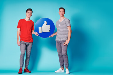 Young friends holding a like notification icon. People, Social media Networking, Messages and technology concept. Blue background.