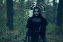 Woman In Image Of Witch Stands In Dark Forest.