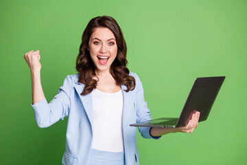 Portrait of smart female worker holding laptop smiling cheerfully wearing blue formal suit isolated on bright green color background