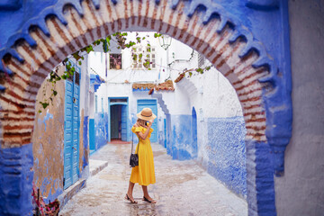 Wall Mural - Colorful traveling by Morocco. Young woman in yellow dress walking in  medina of  blue city Chefchaouen.