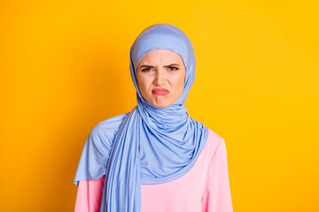 Wall Mural - Close-up portrait of attractive displeased capricious muslimah wearing hijab pursue lips isolated on bright yellow color background