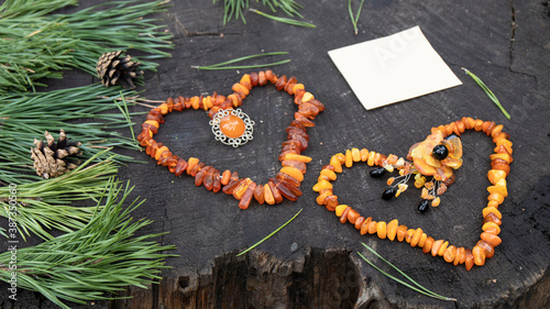 Two vintage Baltic amber necklaces made of honey and milk amber and handmade  brooches are laid out in the shape of a heart on a dark stump. Amber is protection, love, healing, powers, luck, magic.