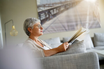 Wall Mural - Senior woman reading newspaper, relaxed in sofa