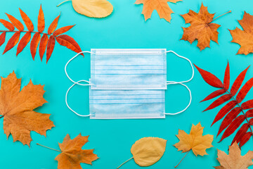 Medical blue masks and leaves on an green background, top view, autumn during pandemic.