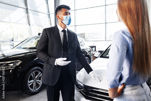 Man car salesman in face mask talking to a client in showroom