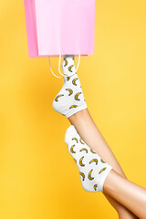 Sticker - Cropped view of woman wearing socks, putting leg in pink paper bag isolated on yellow background