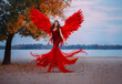 © kharchenkoirina - Young beautiful fantasy woman fallen angel lying in air near a tree with orange leaves. Creative red costume, huge artificial bird wings and elegant dress. magic autumn foliage. Photo of levitation.