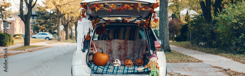 Trick o trunk. White car trunk decorated for Halloween. Autumn fall decor with red pumpkins and yellow leaves for October holiday outdoors. Alternative safe celebration. Web banner header.