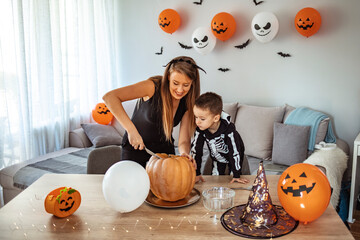 Happy family a cheerful woman and her son are laughing during Halloween celebration at home. Mother and son have a fun with pumpkins at kitchen at home. Happy Halloween concept