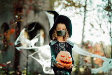 Happy Halloween On Quarantine Coronavirus Pandemic. Social Distance. Child Girl In Witch Halloween Costume Wearing Medicine Mask.
