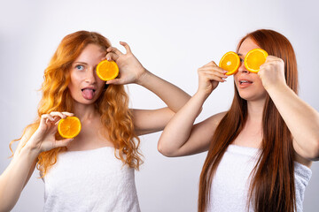 Red-haired girlfriends are having fun and posing with orange slices. Healthy food, spa and beauty, vitamins and happiness concept. Photo on white background