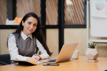 running on a computer laptop on the table. business suit clothing, white shirt. sitting in a modern office coworking, favorite job marketing. office employee of the Bank is a brunette woman.