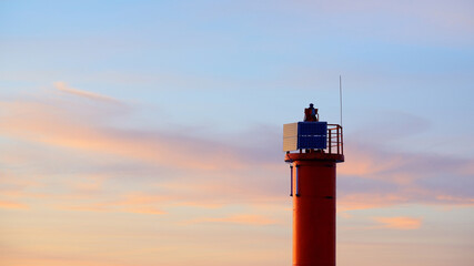 Wall Mural - Orange lighthouse with solar battery against colorful sunset sky, close-up. Stunning cloudscape. Alternative energy and environmental conservation theme. Baltic sea, Riga bay, Latvia
