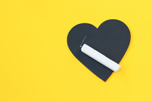 Black Heart Shaped Writing Board And Chalk On Yellow Background With Copy Space