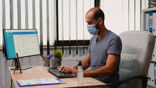 Worker wearing protection mask using sanitiser gel during coronavirus. Entrepreneur working in new normal office workplace in company cleaning hands using antibacterian alcohol against corona virus.