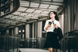 © YiuCheung - A business woman using smartphone and holding coffee on modern steel bridge.