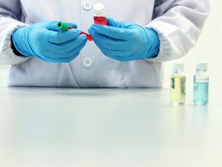 The scientist holding Vial glass bottle with red solvent or solution wear nitrile blue gloves, with colorful cell culture tubes cover with green caps, biotechnology analysis experiment for anti-virus.