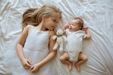 Little sister and her newborn brother. Toddler kid meeting new sibling. Cute girl and new born baby boy relax in a home bedroom. Family with two children at home. Love, trust and tenderness concept