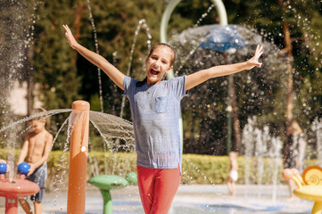 Little funny girl in splashes on water playground