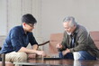 © Akarawut - Senior Asian man playing chess with his son in the living room for elder and family concept
