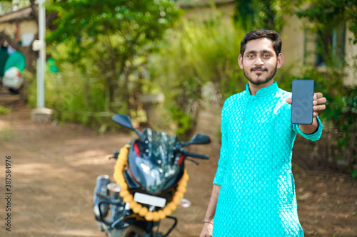 Cuadros en Lienzo Young Indian boy in ethnic wear and showing smartphone with new bike