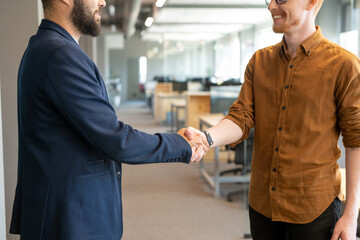 Poster - Handshake of two young male colleagues in casualwear standing in the aisle