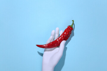 Mannequin hand holding hot chili pepper on blue background