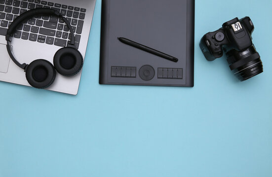 Workspace of a photographer or retoucher. Laptop, graphic tablet, camera and headphones on a blue background. Top view. Copy space