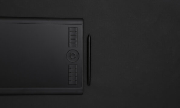 Graphic tablet with pen on black background. Top view